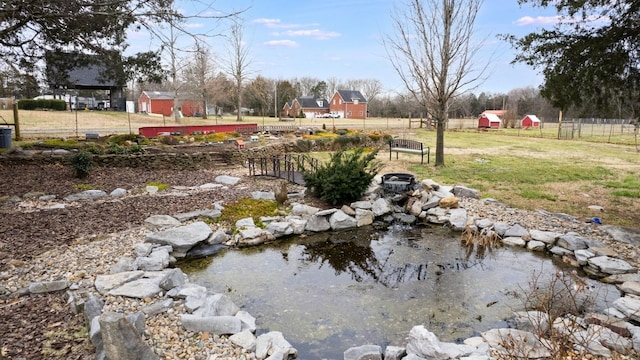 view of yard with an outdoor structure, a small pond, a shed, and fence