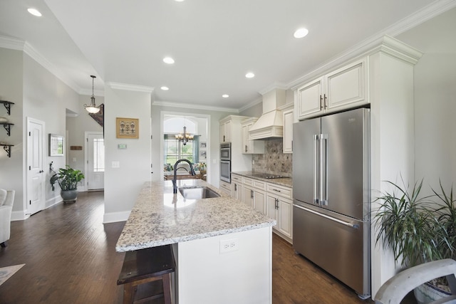 kitchen with a notable chandelier, a sink, premium range hood, stainless steel appliances, and an island with sink