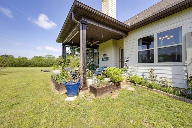 entrance to property featuring a yard, a chimney, and ceiling fan