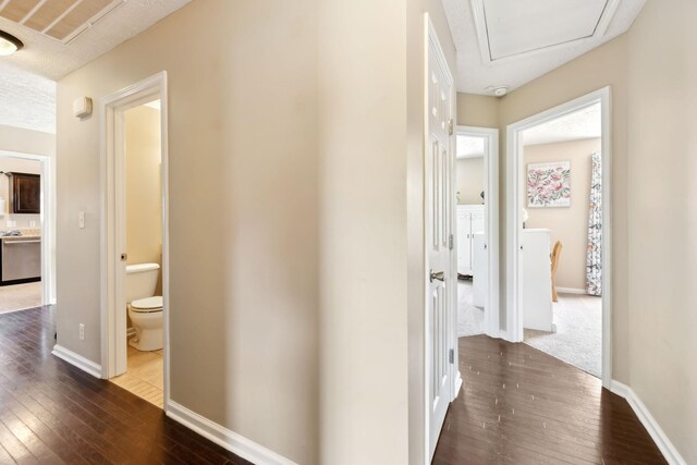 hall with dark wood-type flooring, baseboards, and attic access