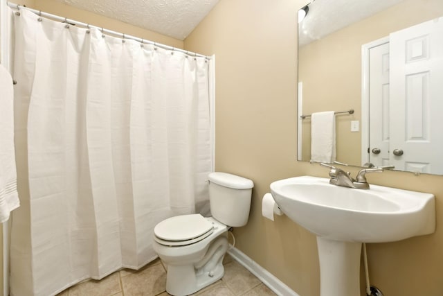 bathroom with tile patterned floors, toilet, baseboards, a textured ceiling, and a sink