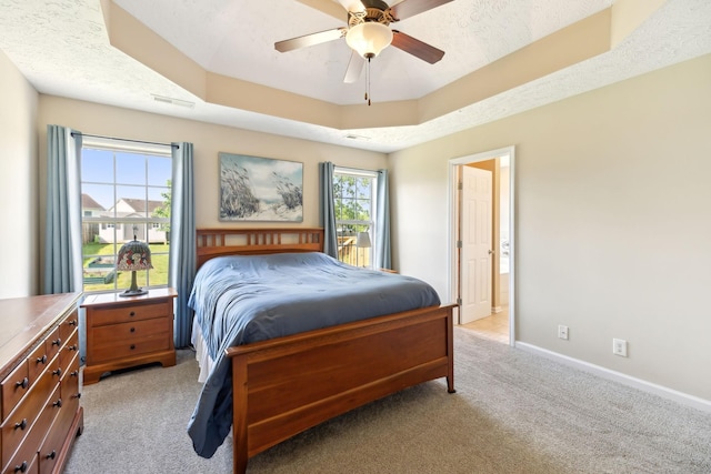 bedroom with light carpet, a raised ceiling, baseboards, and a ceiling fan