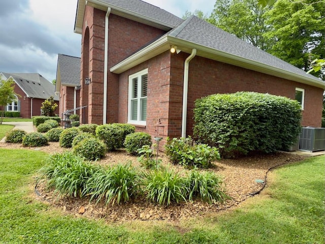 view of home's exterior with central AC unit, a yard, brick siding, and a shingled roof