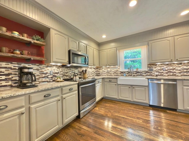 kitchen with a sink, crown molding, dark wood-style flooring, appliances with stainless steel finishes, and decorative backsplash