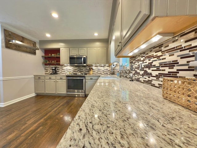 kitchen with light stone countertops, a sink, backsplash, appliances with stainless steel finishes, and dark wood-style floors