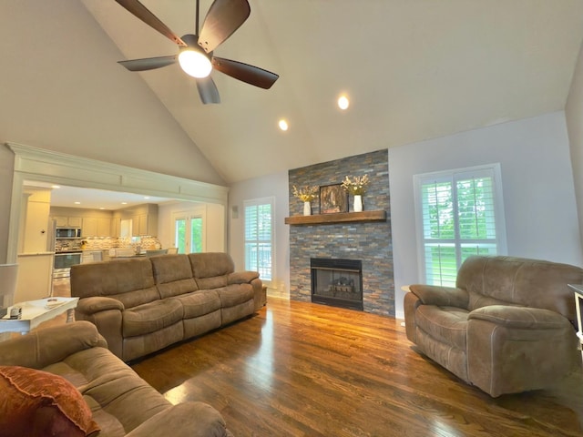 living area with wood finished floors, high vaulted ceiling, a fireplace, a wealth of natural light, and a ceiling fan