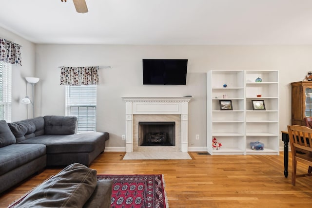 living room with baseboards, a high end fireplace, ceiling fan, and wood finished floors