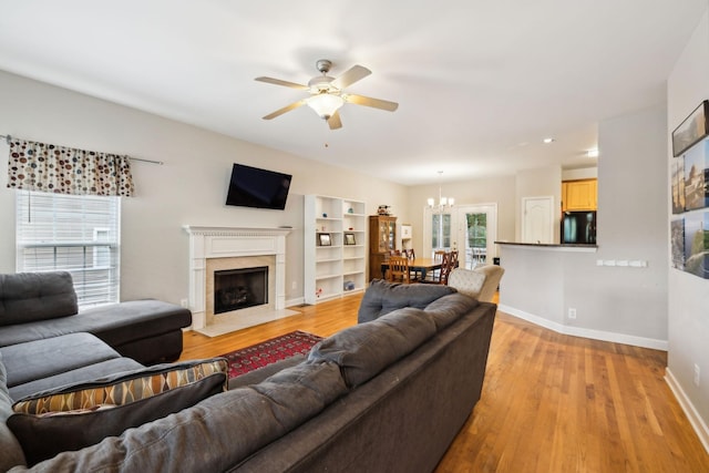 living room featuring baseboards, a wealth of natural light, light wood-style floors, and ceiling fan with notable chandelier
