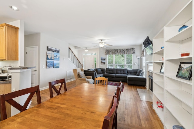 dining area with light wood-style floors, stairway, a ceiling fan, and a fireplace with flush hearth