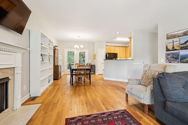 living area featuring baseboards, a fireplace, an inviting chandelier, and light wood-type flooring