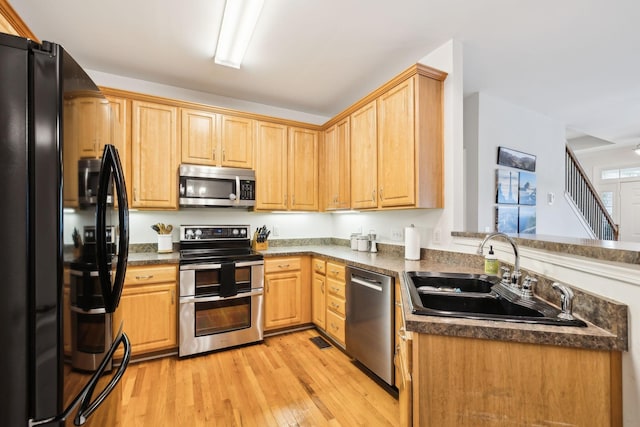 kitchen with a sink, a peninsula, stainless steel appliances, dark countertops, and light wood-style floors