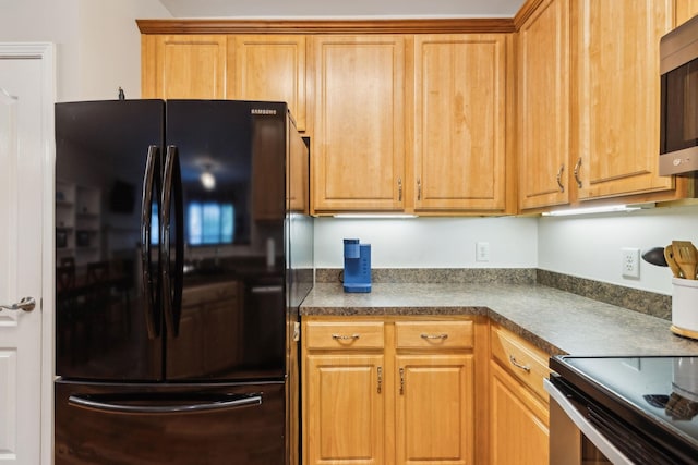 kitchen with freestanding refrigerator, brown cabinetry, stainless steel microwave, dark countertops, and range with electric stovetop