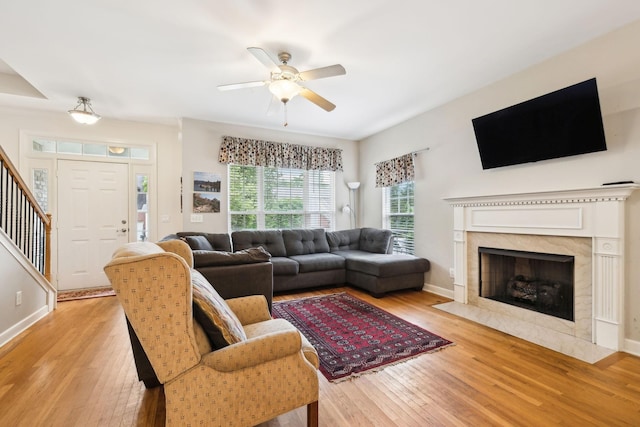 living room with baseboards, a high end fireplace, light wood-type flooring, and a ceiling fan