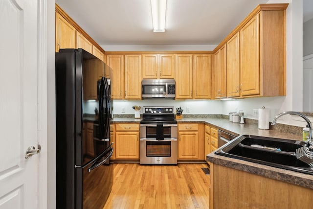kitchen with light wood finished floors, dark countertops, stainless steel appliances, and a sink