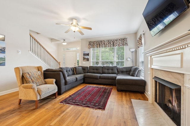 living area with a ceiling fan, a premium fireplace, baseboards, stairs, and hardwood / wood-style floors