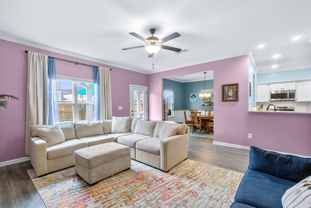 living area with baseboards, ceiling fan with notable chandelier, crown molding, and wood finished floors