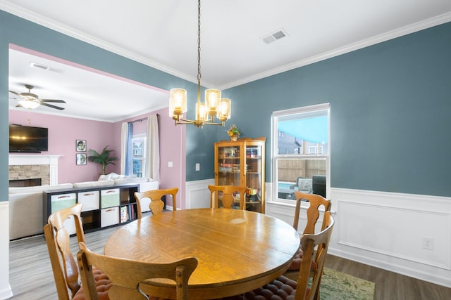 dining room featuring crown molding, a stone fireplace, visible vents, and wood finished floors