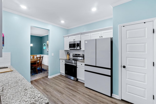 kitchen featuring appliances with stainless steel finishes, ornamental molding, white cabinetry, backsplash, and light wood-style floors