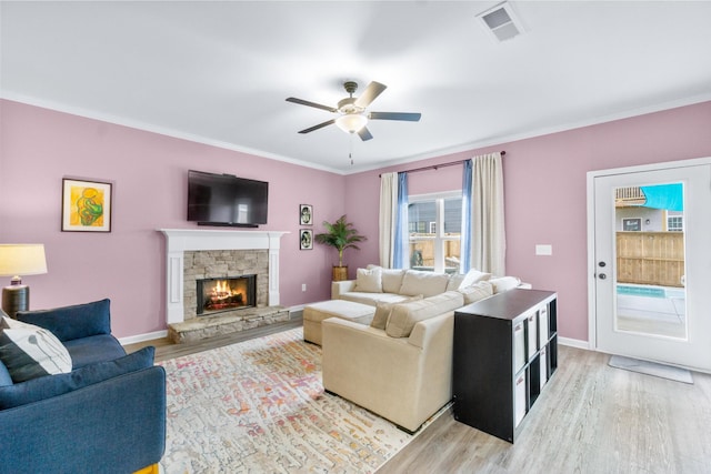 living area with ceiling fan, a stone fireplace, light wood-type flooring, and visible vents