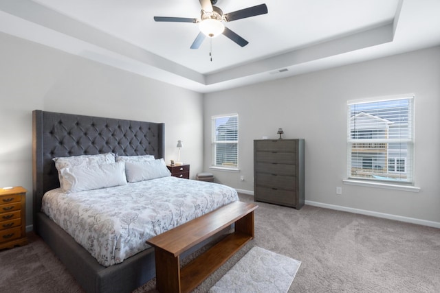 bedroom with carpet, a tray ceiling, visible vents, baseboards, and ceiling fan