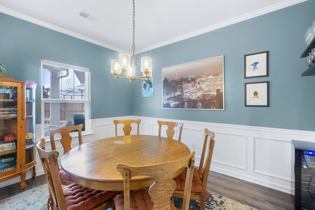 dining room with wood finished floors, ornamental molding, visible vents, a chandelier, and wainscoting