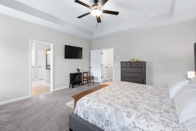 carpeted bedroom featuring a wood stove, a raised ceiling, connected bathroom, and baseboards