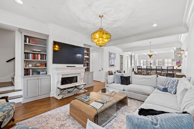 living area with ornamental molding, a notable chandelier, a fireplace with flush hearth, and wood finished floors
