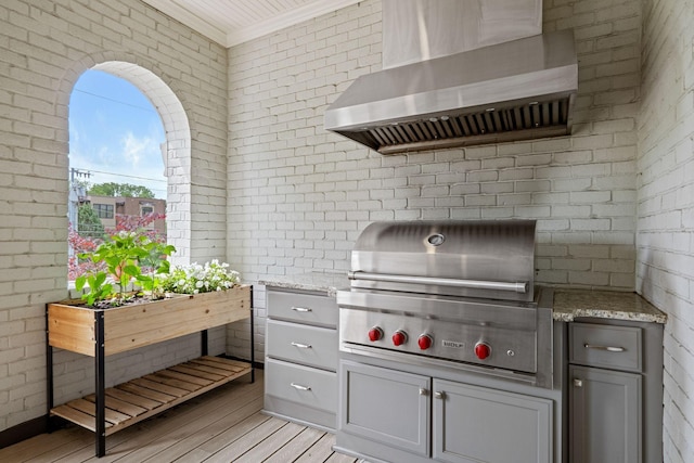 kitchen featuring light wood-style floors, ornamental molding, light stone counters, and wall chimney exhaust hood