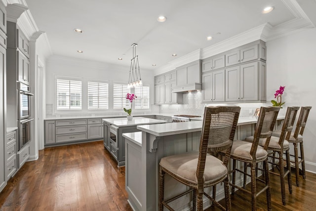 kitchen with a breakfast bar, stainless steel double oven, backsplash, light countertops, and gray cabinetry