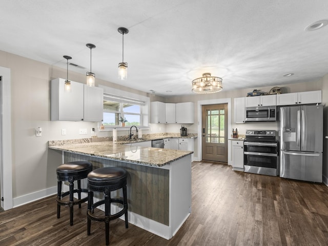 kitchen with baseboards, light stone counters, a sink, a peninsula, and appliances with stainless steel finishes