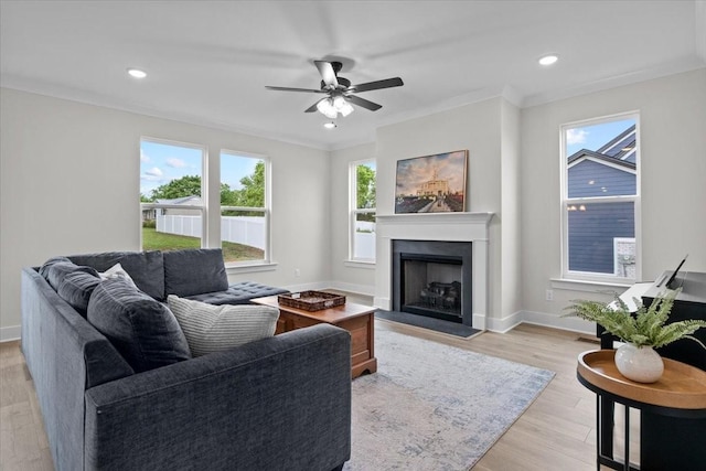 living area featuring baseboards, ornamental molding, ceiling fan, a fireplace, and light wood-type flooring