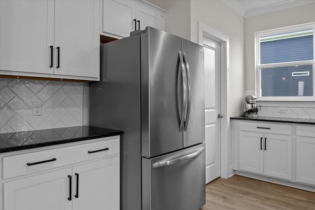 kitchen featuring freestanding refrigerator, tasteful backsplash, white cabinets, light wood-style floors, and dark stone counters