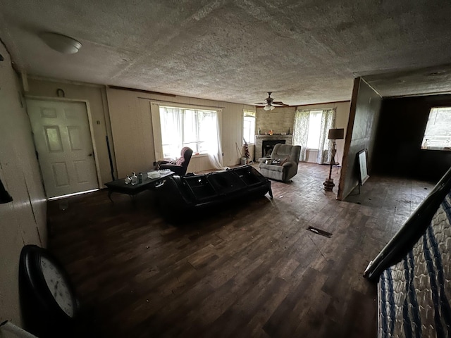 living area featuring a fireplace, ceiling fan, a textured ceiling, and wood finished floors