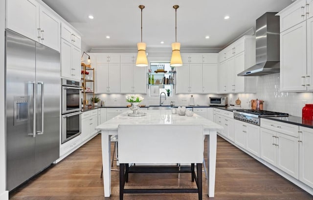 kitchen featuring a sink, stainless steel appliances, wall chimney range hood, white cabinetry, and decorative backsplash