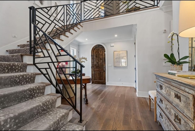 entrance foyer with baseboards, crown molding, wood finished floors, arched walkways, and stairway