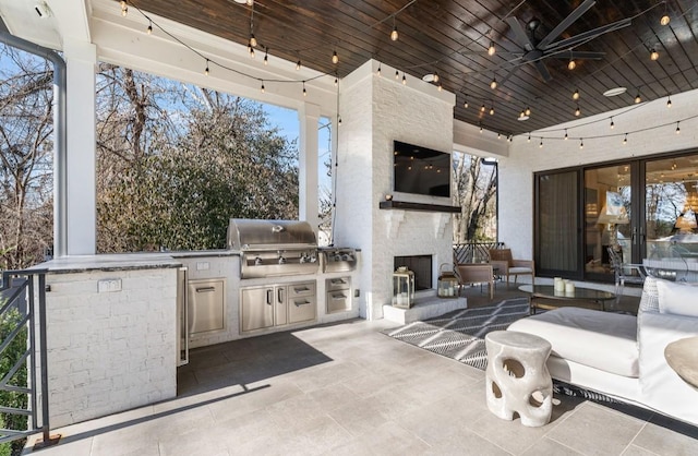 view of patio / terrace with a grill, ceiling fan, an outdoor living space with a fireplace, and exterior kitchen