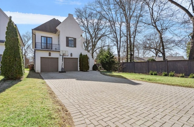 view of front of home featuring a balcony, fence, a garage, stucco siding, and a front yard