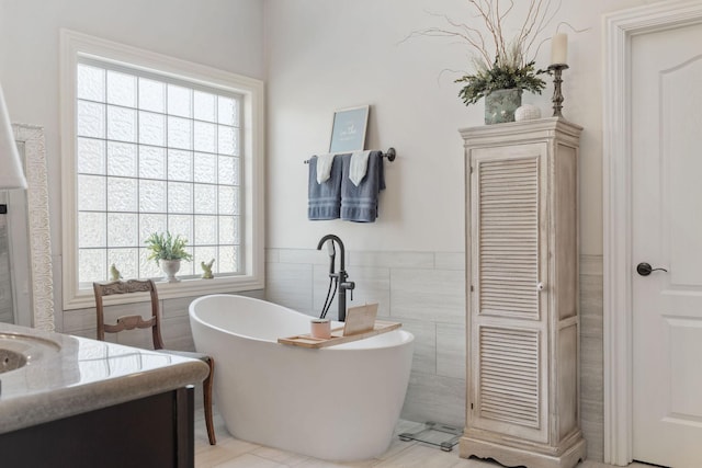 bathroom featuring a soaking tub, tile walls, a wainscoted wall, and vanity