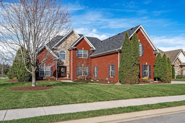 traditional-style home featuring a front yard, roof with shingles, and brick siding
