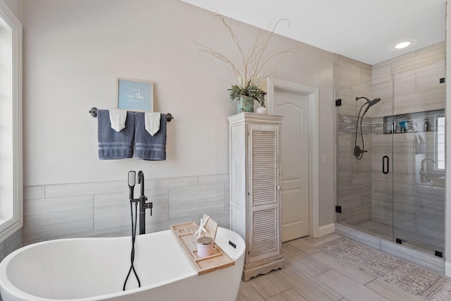 bathroom featuring a stall shower, a freestanding bath, and tile walls