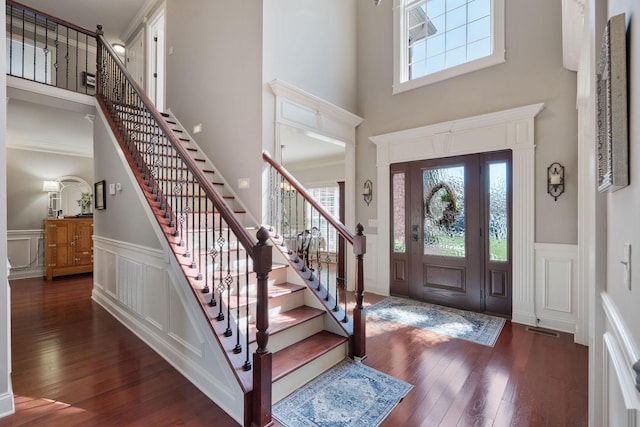 foyer with visible vents, a decorative wall, wood-type flooring, and a towering ceiling