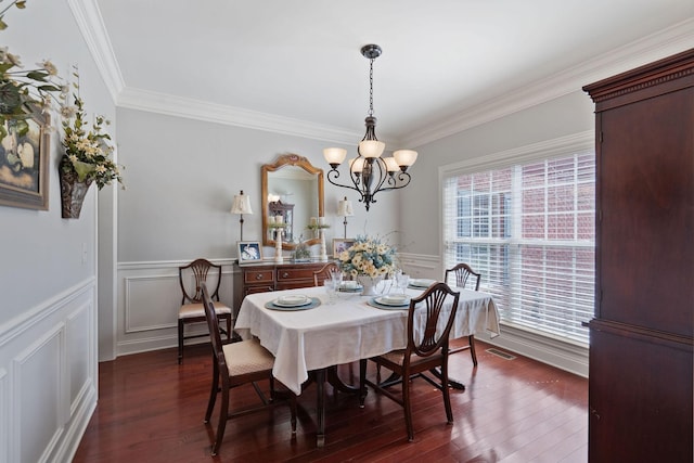 dining room featuring dark wood-style flooring, an inviting chandelier, crown molding, and a wainscoted wall