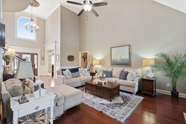 living room with baseboards, ornamental molding, ceiling fan with notable chandelier, a towering ceiling, and wood finished floors