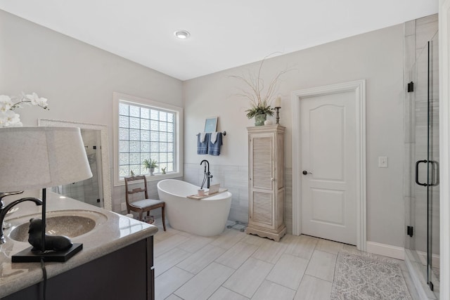 full bath featuring a freestanding bath, vanity, tile walls, and a shower stall