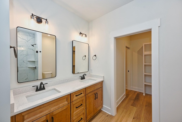 full bathroom with a shower, double vanity, a sink, and wood finished floors