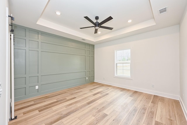 unfurnished room with a decorative wall, visible vents, light wood-style flooring, a ceiling fan, and a raised ceiling