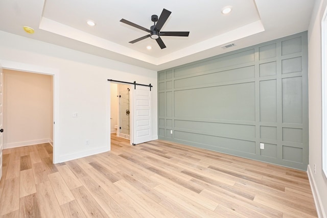 unfurnished bedroom featuring a raised ceiling, a decorative wall, and a barn door