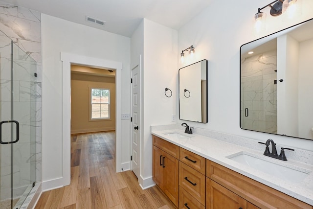 full bathroom featuring a marble finish shower, visible vents, wood finished floors, and a sink