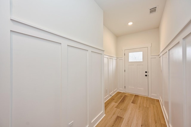 doorway to outside featuring light wood-style flooring, visible vents, a decorative wall, wainscoting, and recessed lighting