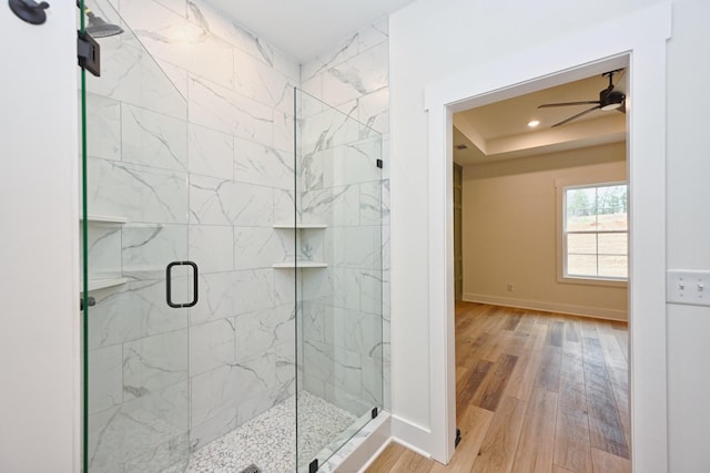 bathroom featuring wood finished floors, baseboards, a raised ceiling, a shower stall, and ceiling fan